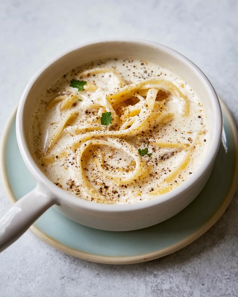 Close-up of pasta coated in creamy Best Alfredo Sauce Recipe Ever, topped with cracked black pepper and parsley.