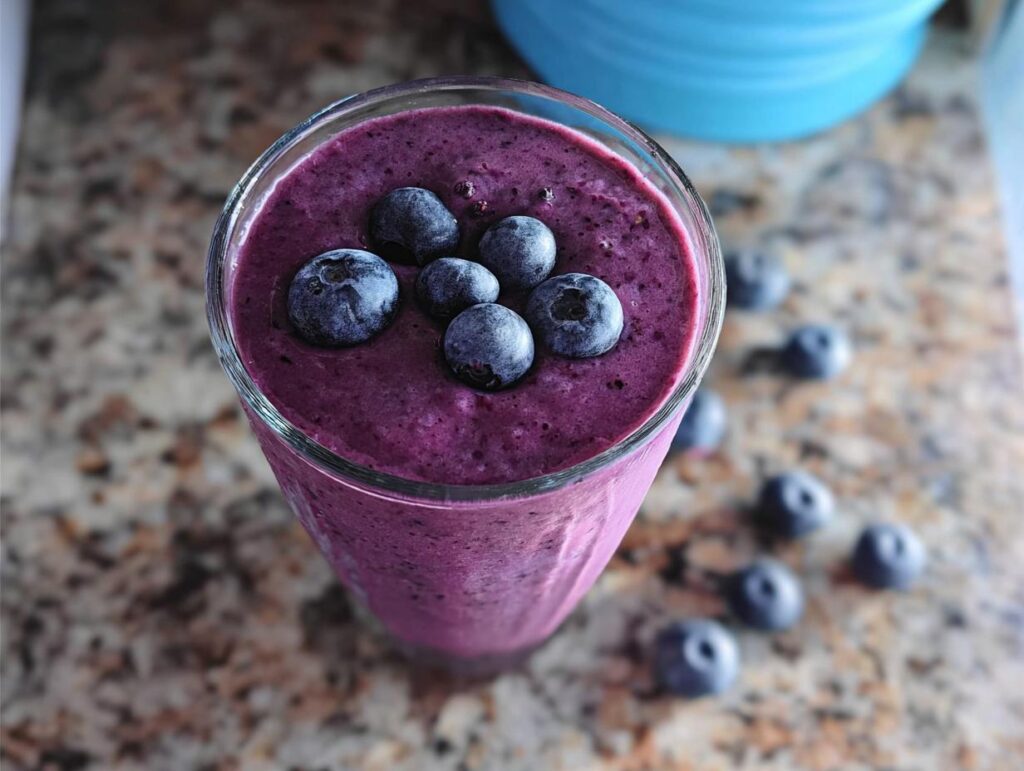 Close-up of a vibrant purple Blueberry Oat Breakfast Smoothie topped with fresh blueberries.