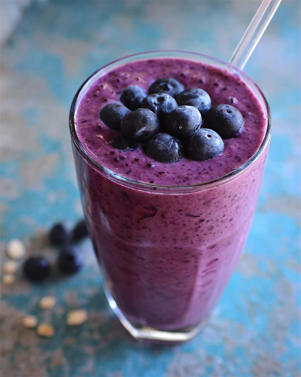 Close-up of a thick, purple Blueberry Oat Breakfast Smoothie topped with fresh blueberries in a glass.