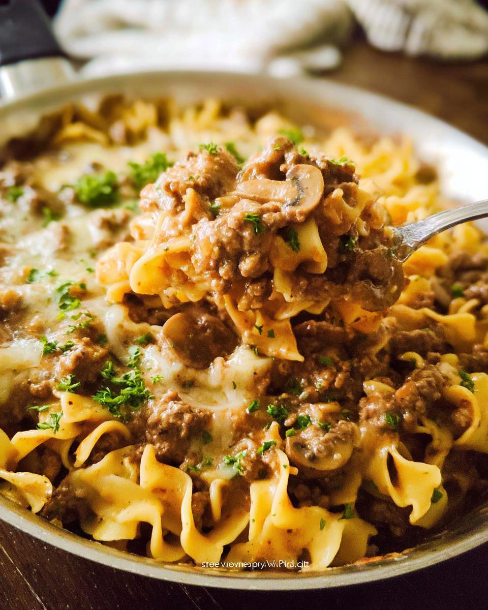 A spoonful of creamy ground beef, mushrooms, and egg noodles, topped with melted cheese, ready to be served from the pan.