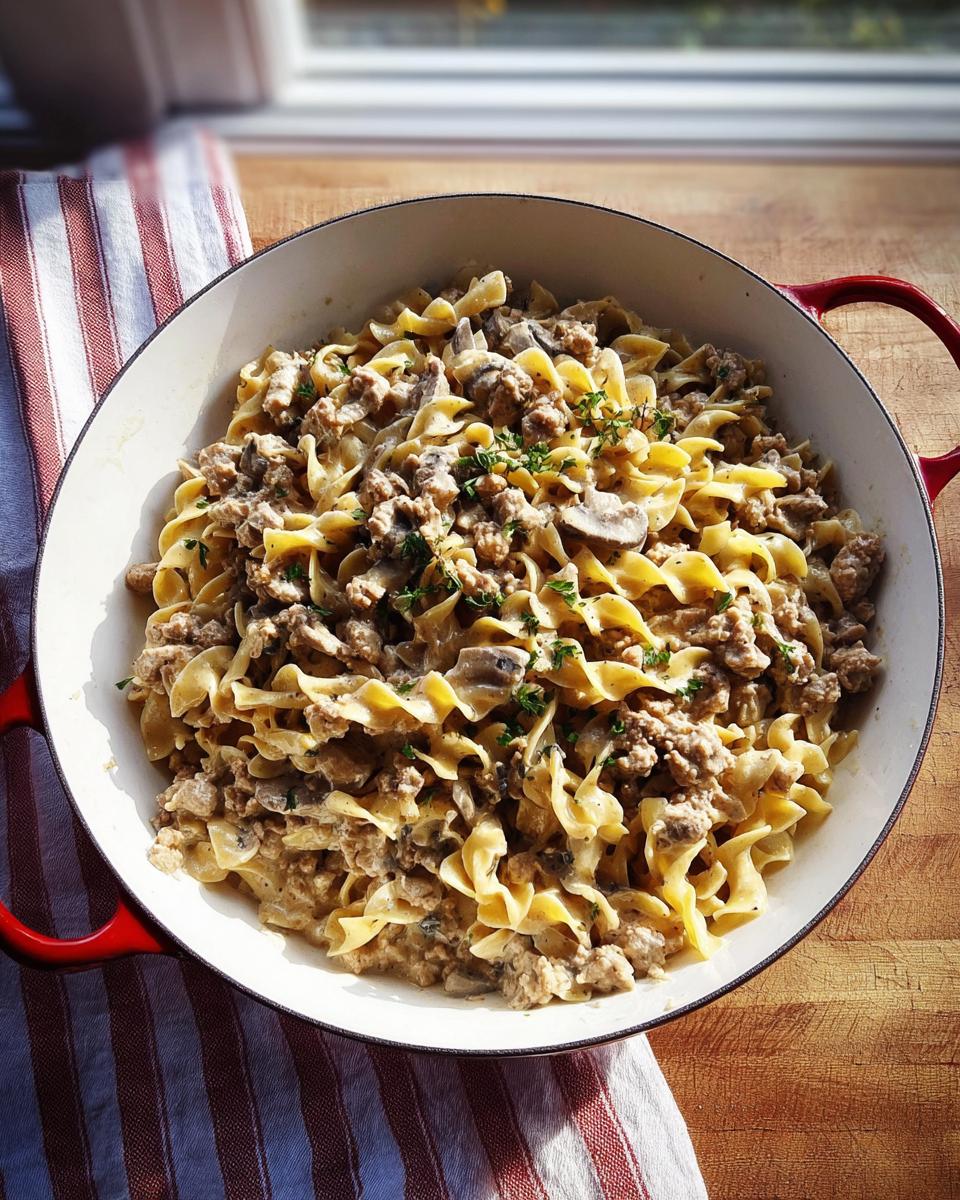A large pot filled with Creamy Turkey Stroganoff and wide egg noodles, garnished with fresh herbs.
