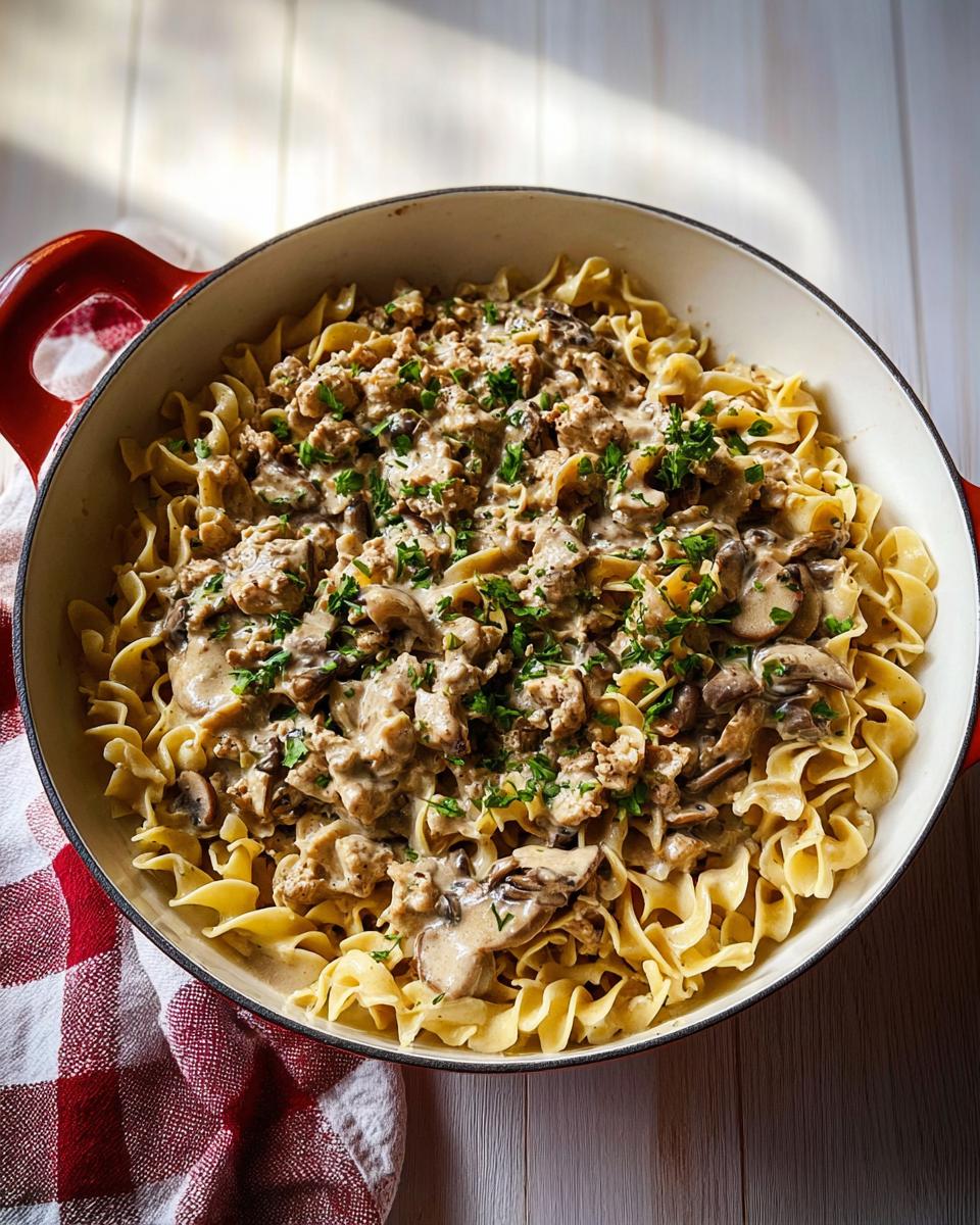 A close-up overhead view of a pot filled with Creamy Turkey Stroganoff served over egg noodles, garnished with fresh parsley.