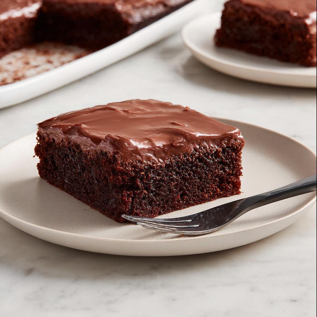 A moist square slice of Easy Snacking Sheet Cake topped with glossy chocolate frosting, served on a plate.