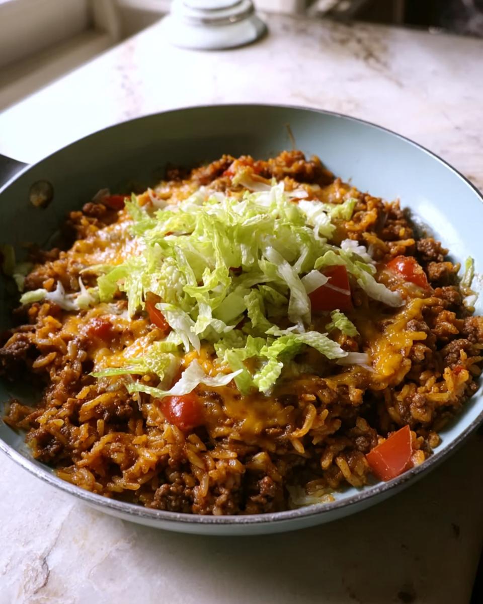 Close-up of a finished Taco Skillet with seasoned ground beef, rice, melted cheese, diced tomatoes, and shredded lettuce.