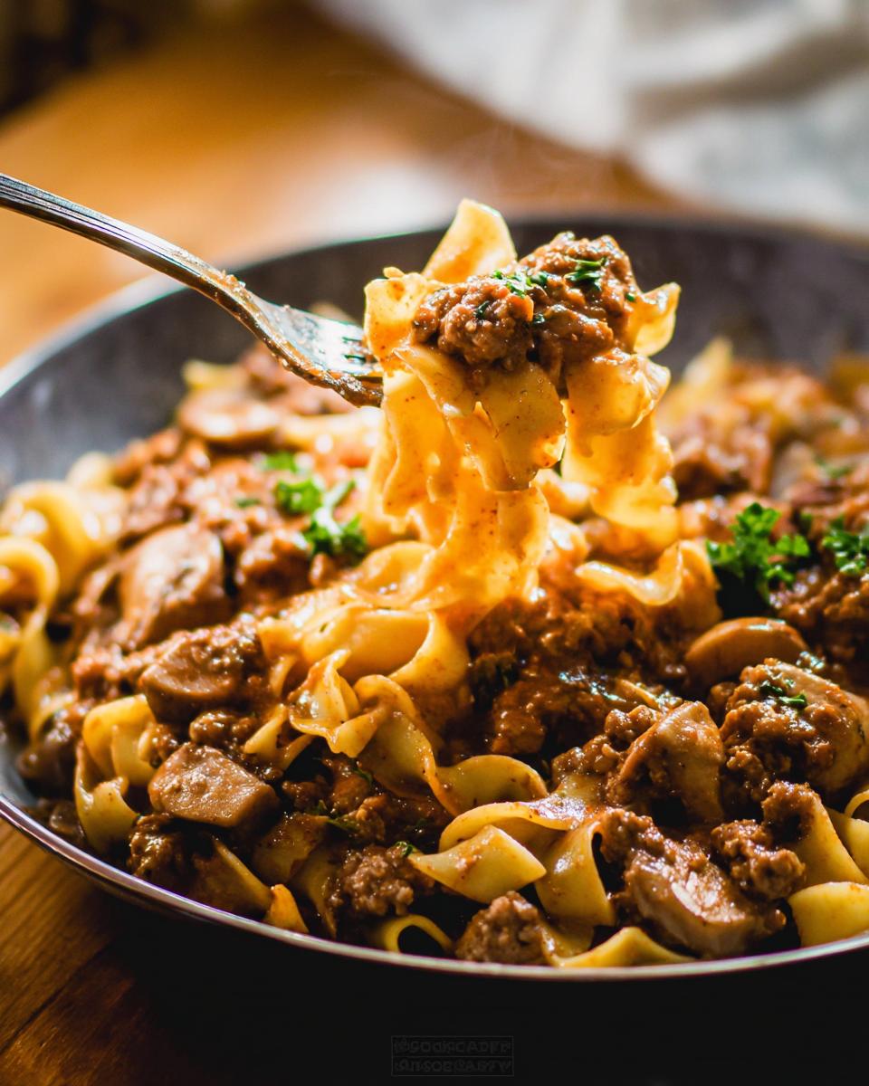 A fork lifts wide noodles coated in a rich, meaty sauce, unlike a typical Beef Enchilada Casserole.