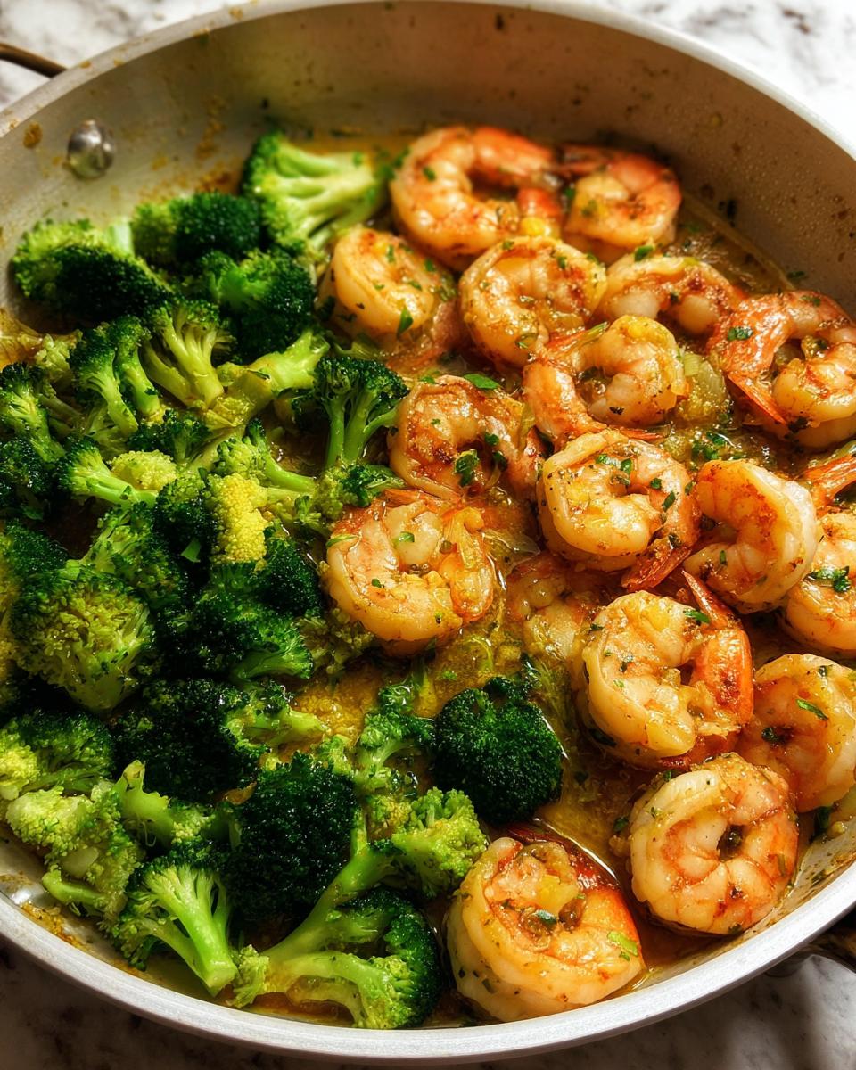 Close-up of Garlic Butter Shrimp & Broccoli cooked in a skillet, with vibrant green broccoli florets and pink shrimp in a glossy sauce.