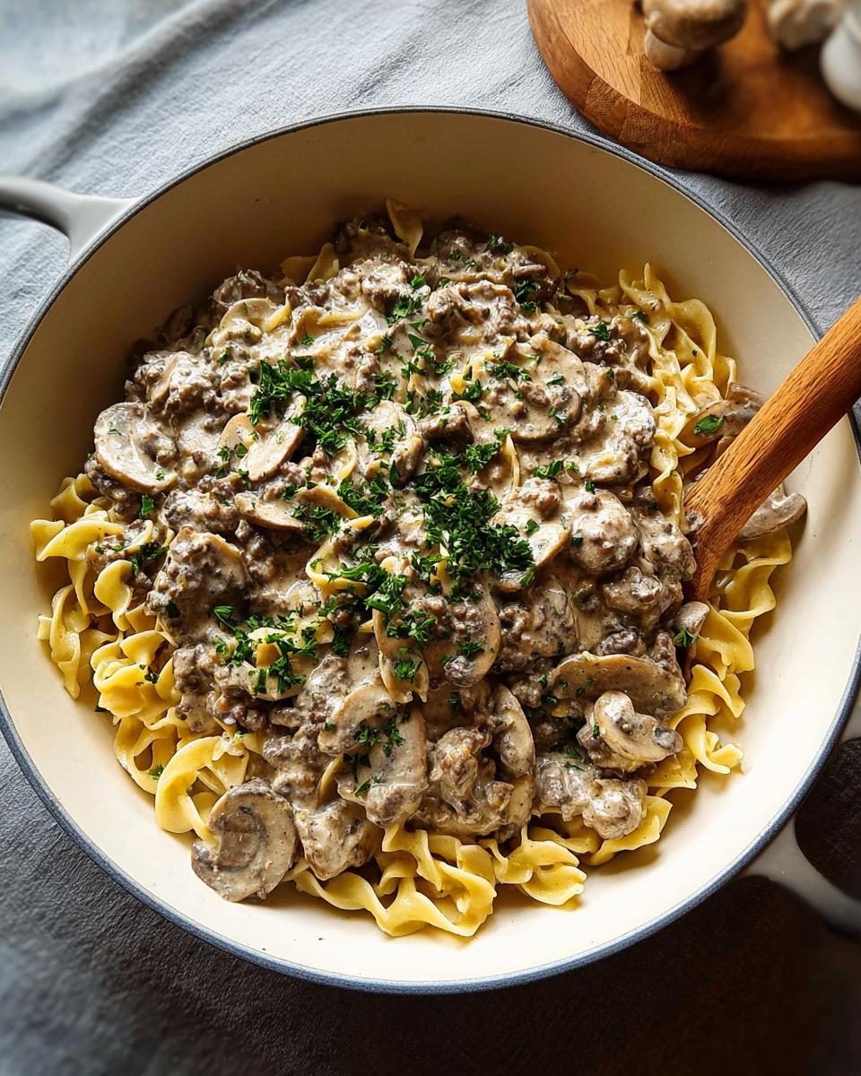 A skillet filled with creamy Ground Beef Stroganoff served over wide egg noodles and garnished with fresh parsley.