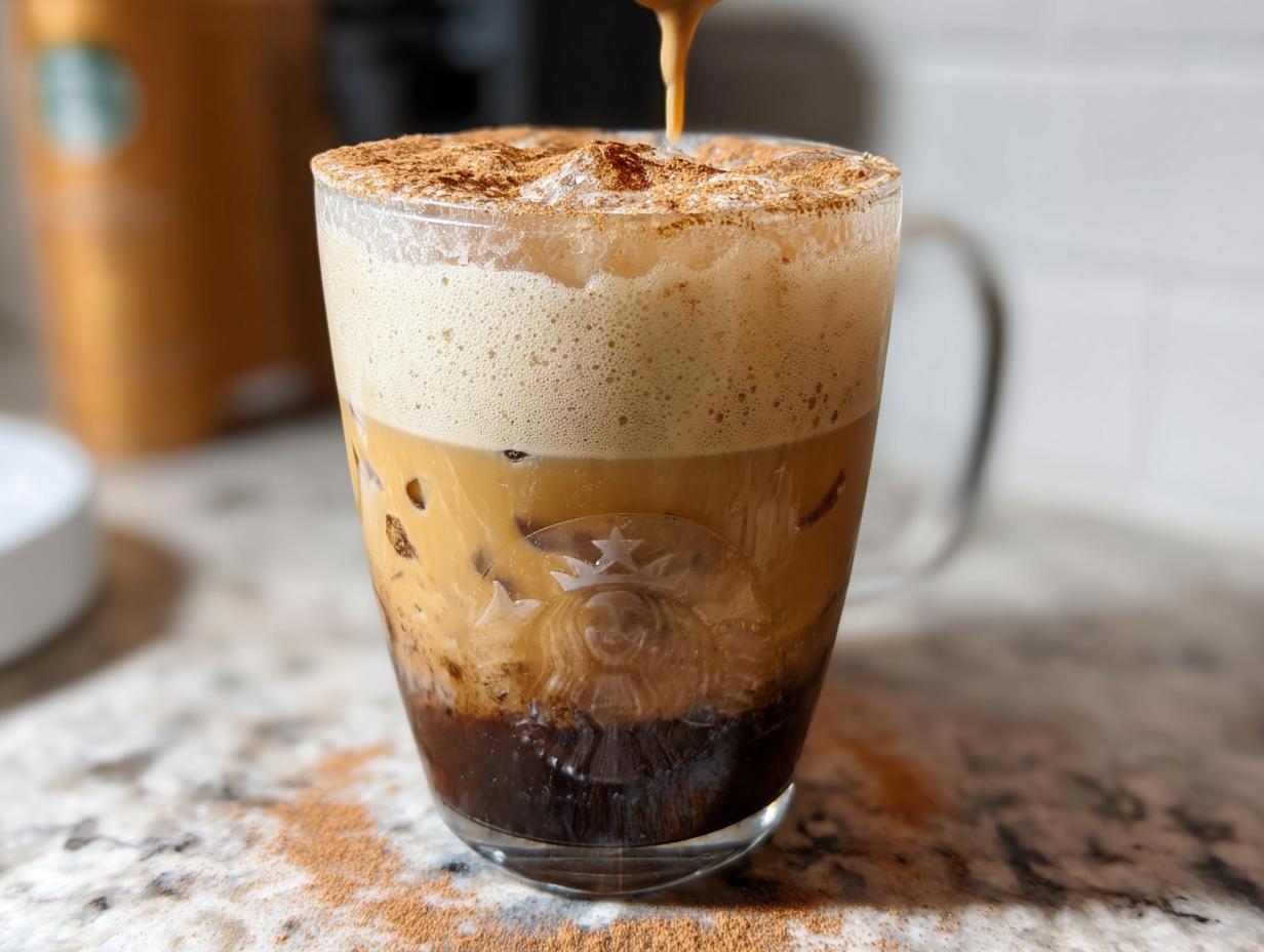 Close-up of a layered Iced Brown Sugar Oatmilk Shaken Espresso being topped with foam and cinnamon.