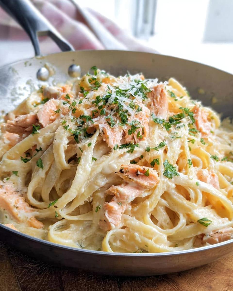 Close-up of Light & Creamy Salmon Pasta with flaked salmon and fresh parsley in a metal skillet.