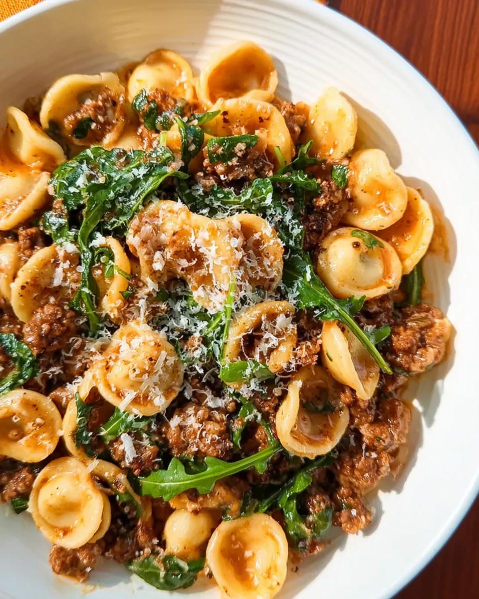 Close-up of a bowl of orecchiette pasta with crumbled sausage, arugula, and grated Parmesan cheese, a perfect dinner idea.