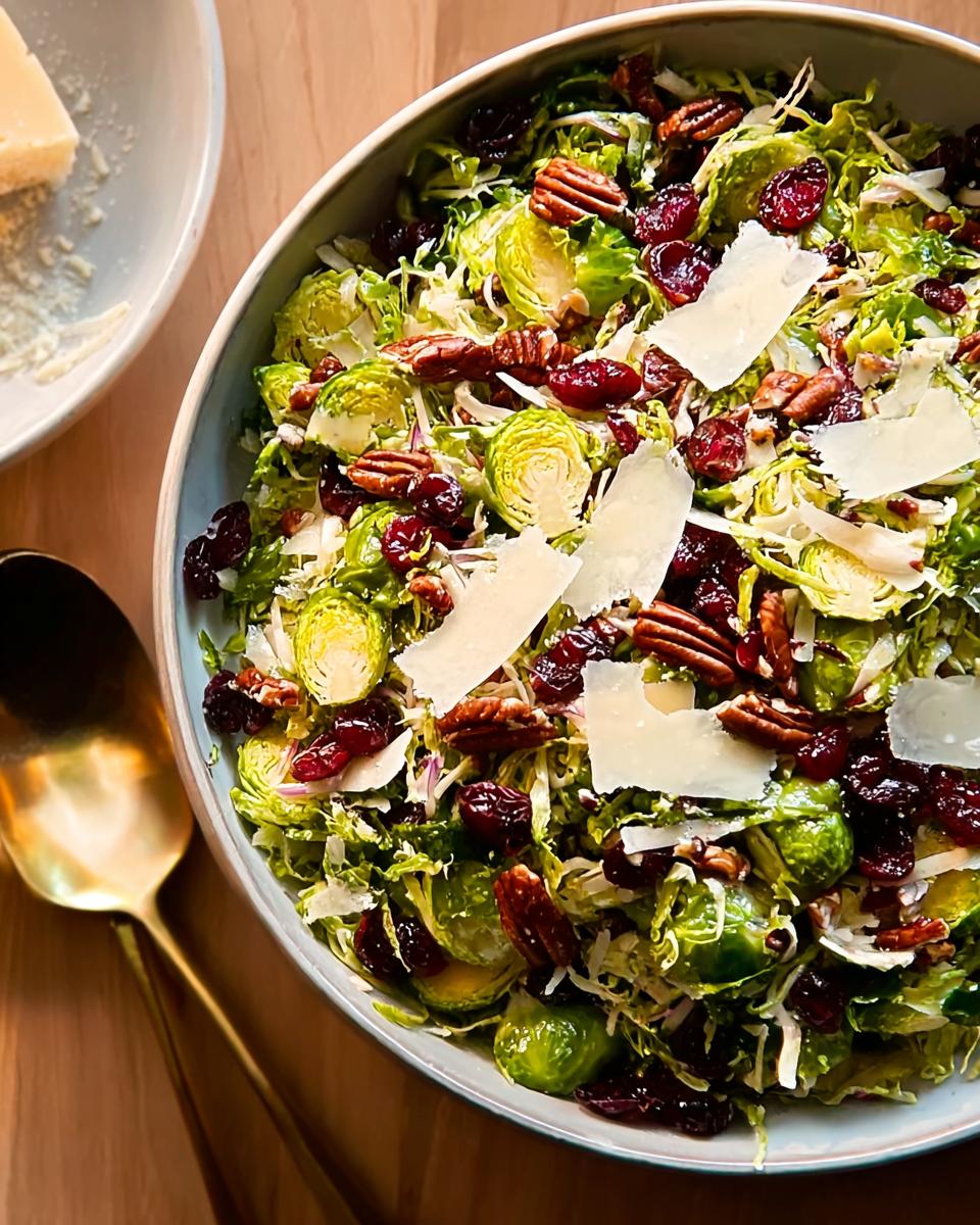 A vibrant bowl of One-Pan Thanksgiving Salad featuring shredded Brussels sprouts, dried cranberries, pecans, and shaved Parmesan cheese.