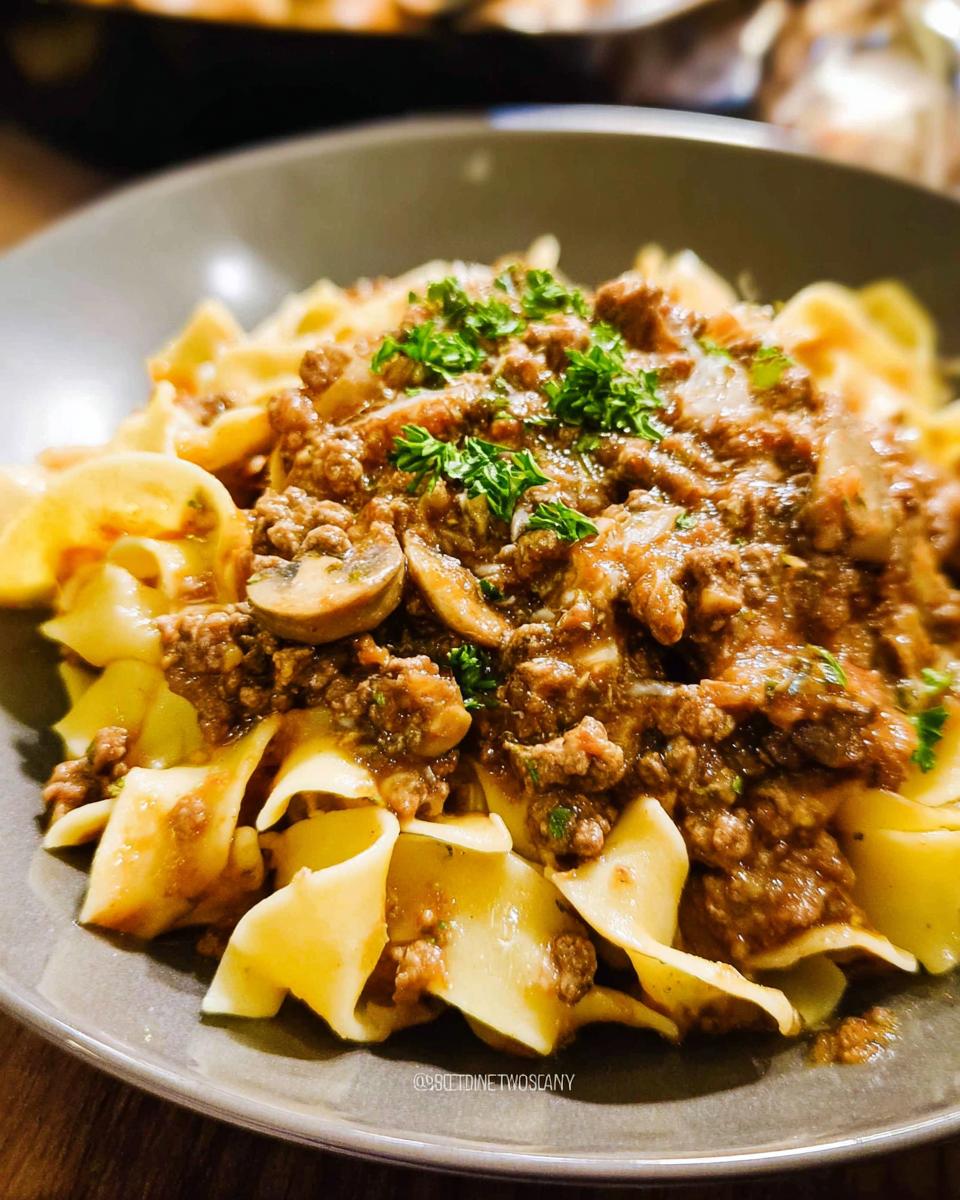 Close-up of wide egg noodles topped with a rich meat sauce containing mushrooms and parsley, despite the article being about Beef Enchilada Casserole.