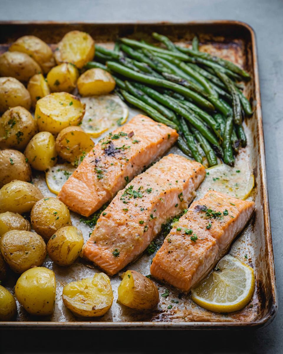 Three perfectly cooked salmon fillets with roasted potatoes and green beans on a sheet pan, a delicious Sheet-Pan Salmon & Veggies meal.