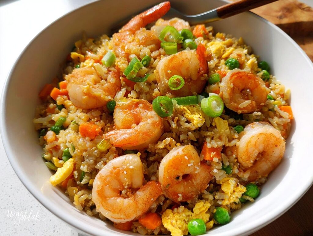 A close-up of a bowl filled with healthy Shrimp Fried Rice, featuring plump shrimp, peas, carrots, and scrambled egg.