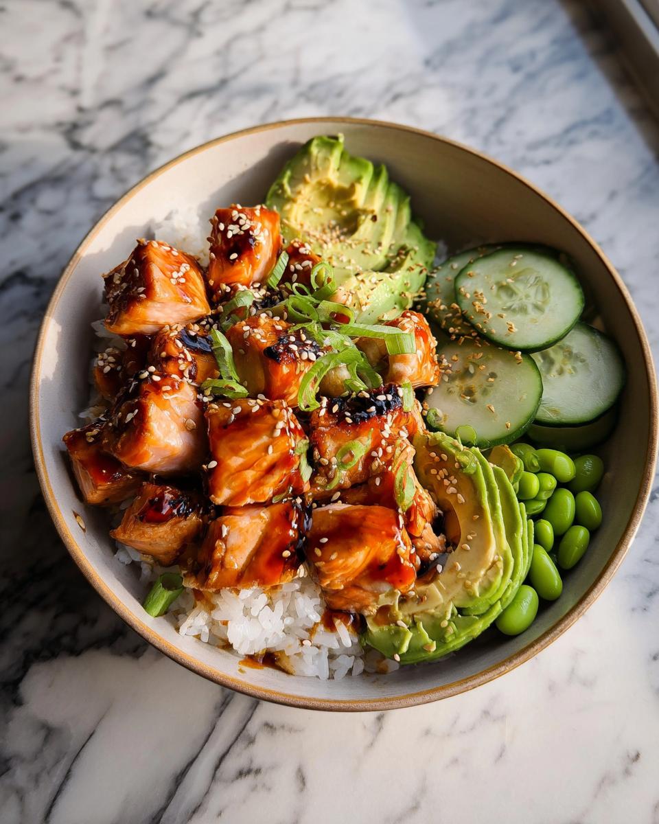 Close-up of a Teriyaki Salmon Bowls featuring glazed salmon chunks over rice, topped with avocado, cucumber, and sesame seeds.