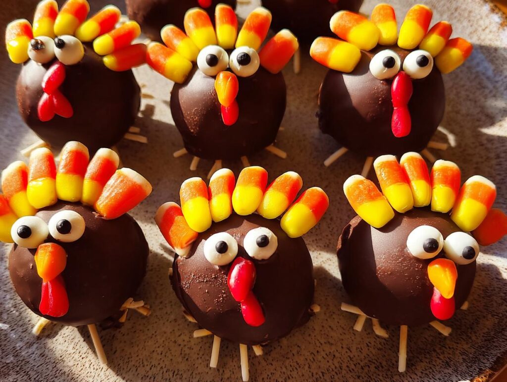 Close-up of chocolate-covered cake pops decorated as turkeys, featuring candy corn feathers and candy eyes, perfect for Thanksgiving desserts.