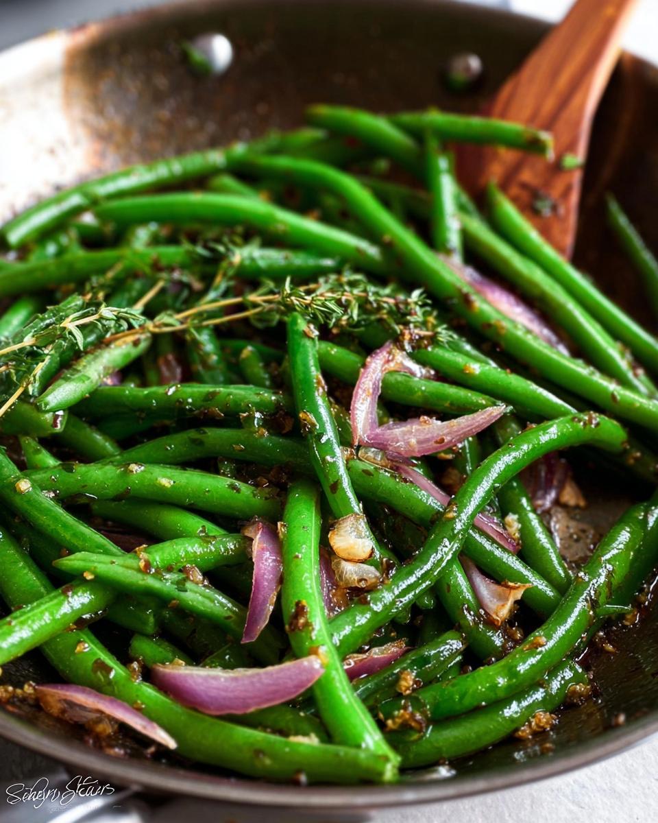 Close-up of Thanksgiving green beans with red onion and thyme being stirred in a pan.