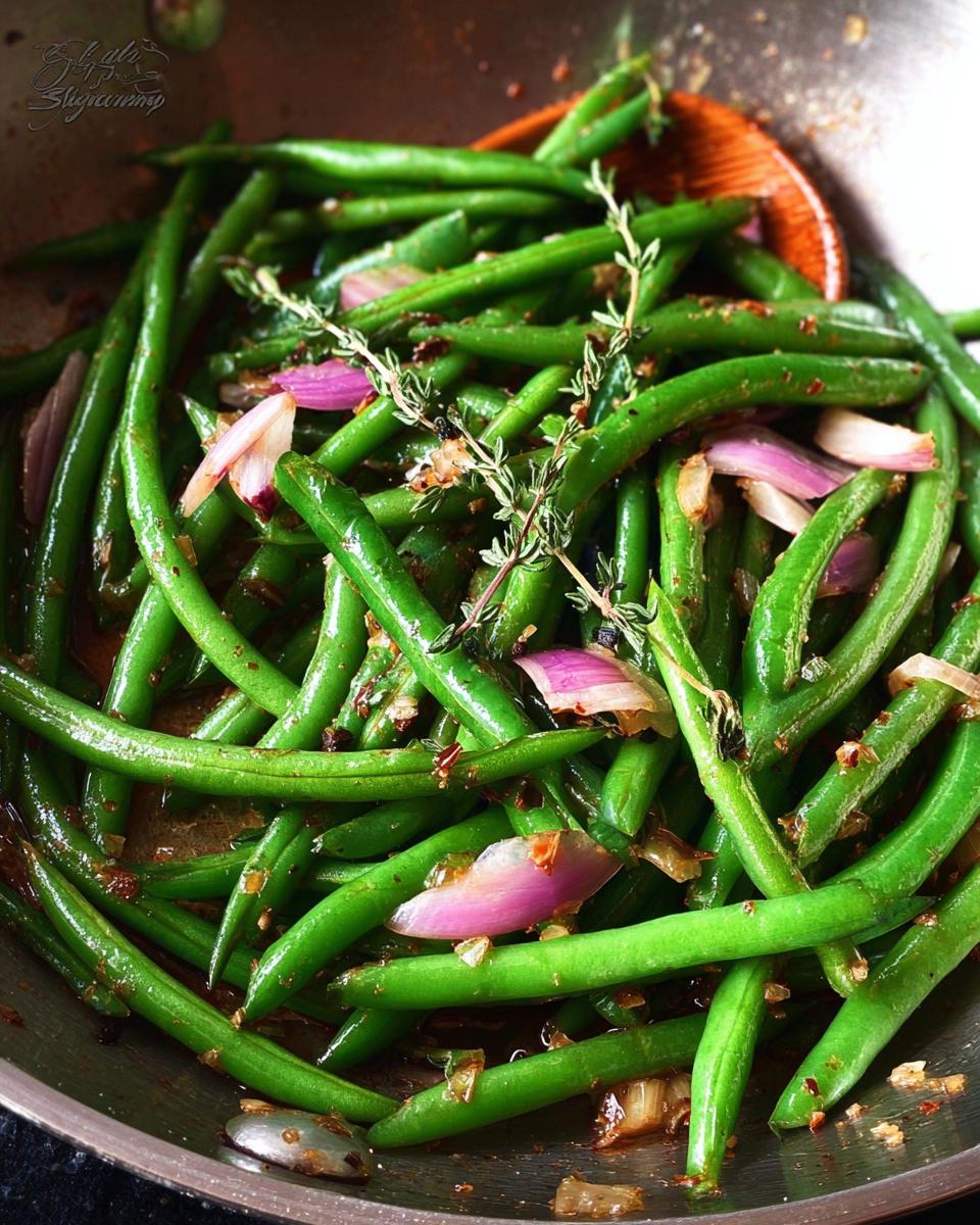 Close-up of Thanksgiving green beans cooked with red onion and thyme in a pan.