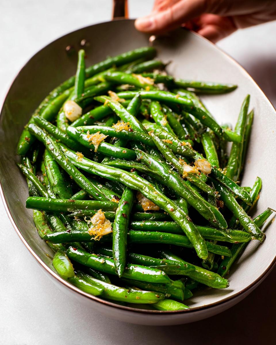 Close-up of glossy, perfectly cooked Thanksgiving green beans with garlic and lemon zest in a serving dish.