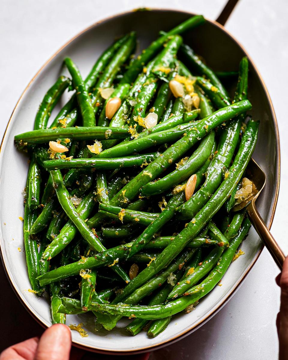 A close-up shot of Thanksgiving green beans tossed with lemon zest and pine nuts in a serving dish.