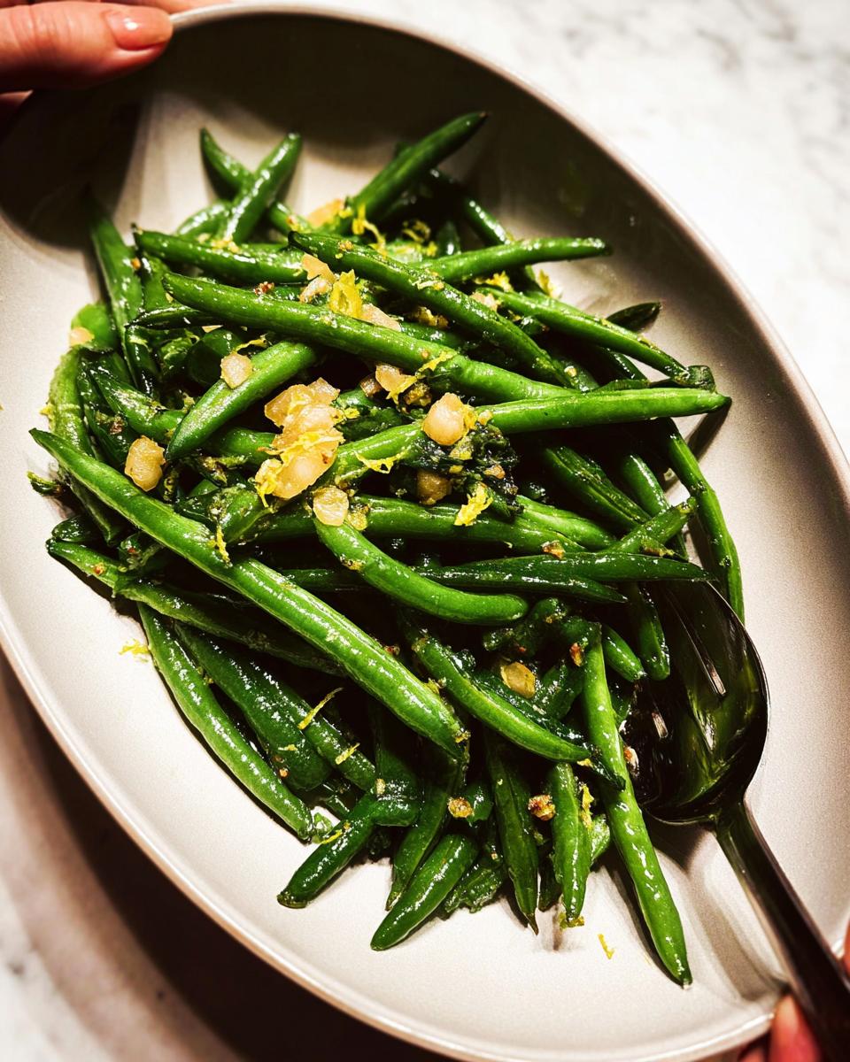 A close-up of bright green Thanksgiving green beans tossed with lemon zest and herbs in a serving dish.