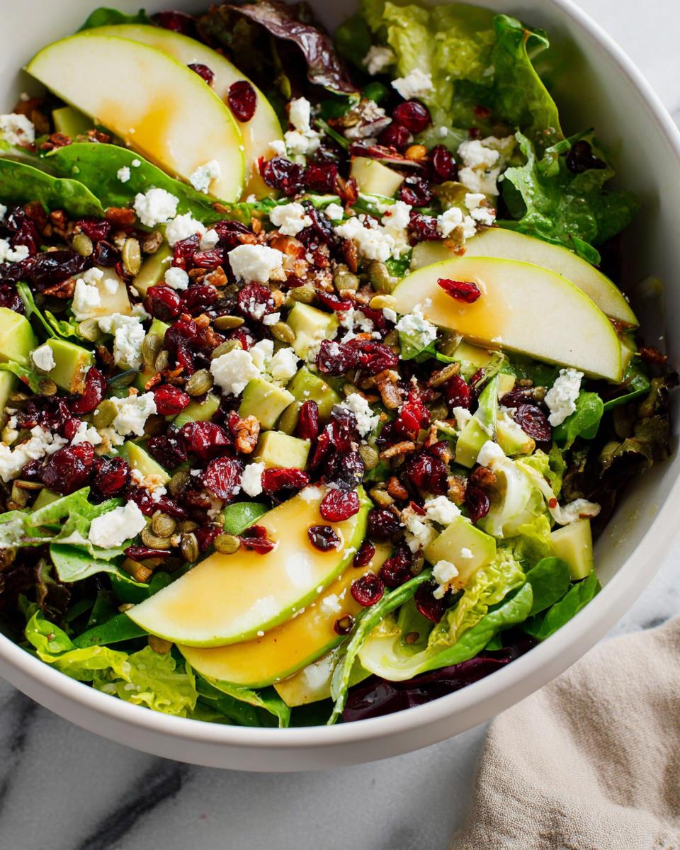 A vibrant Thanksgiving salad with fresh lettuce, sliced apples, dried cranberries, crumbled feta, and a light dressing.