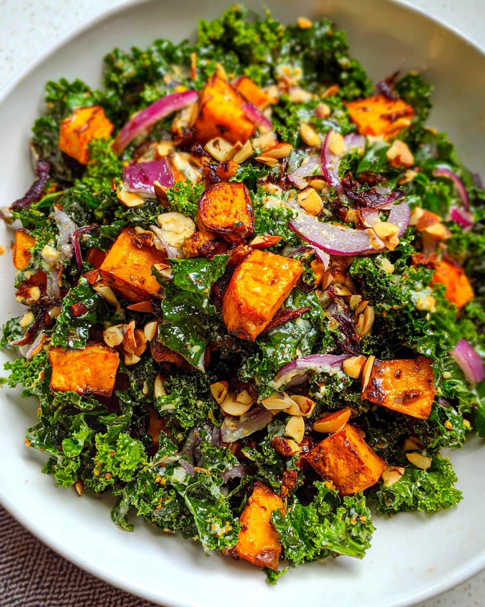 A vibrant Thanksgiving salad featuring massaged kale, roasted sweet potato cubes, red onion, and slivered almonds.