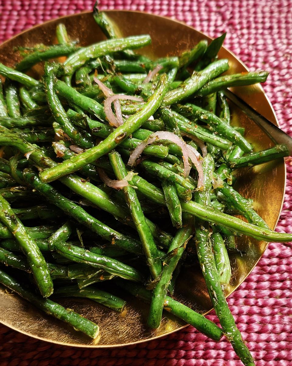 Close-up of a golden bowl filled with glistening green beans, seasoned and topped with slivers of red onion.