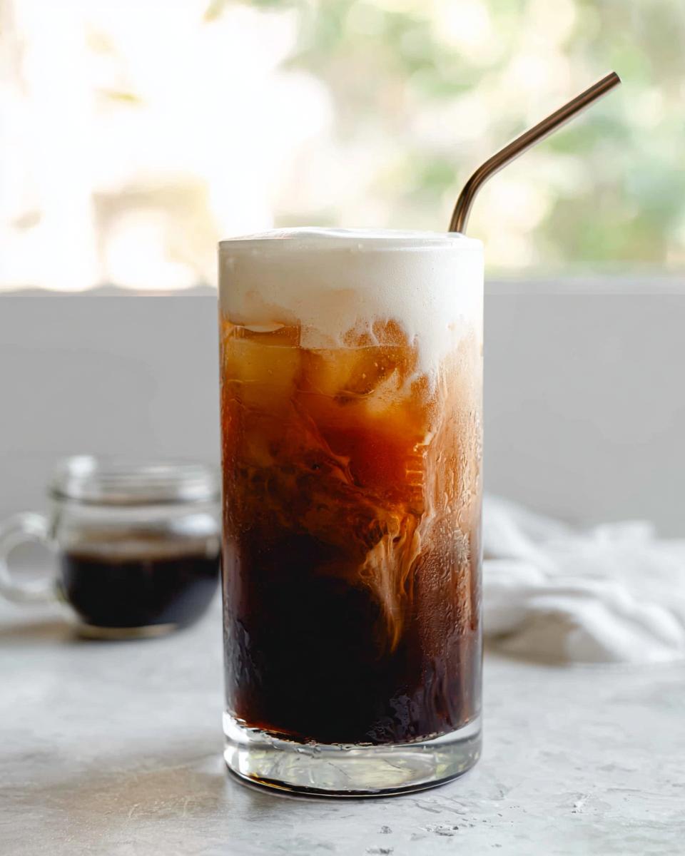 A tall glass of Vanilla Sweet Cream Cold Foam Cold Brew with ice, showing the creamy foam topping and swirling cold brew.