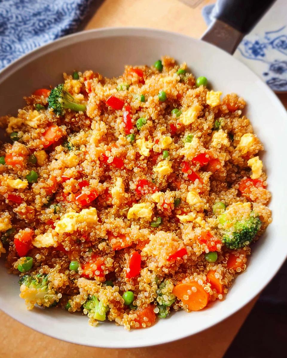 Close-up of colorful Vegetable Quinoa Fried Rice with scrambled egg, peas, carrots, and broccoli in a light-colored pan.