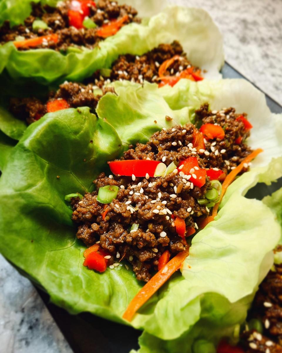 Close-up of Asian Ground Beef Lettuce Wraps filled with savory ground meat, topped with sesame seeds, red peppers, and carrots.