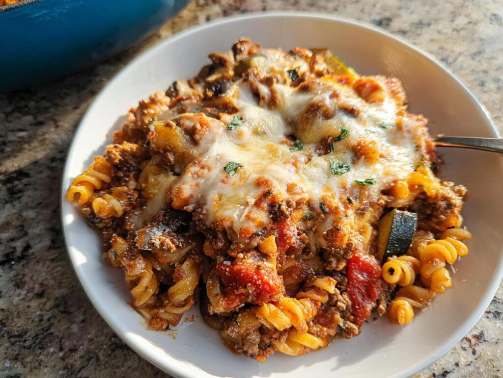 A serving of Cheesy Ground Beef Pasta Skillet featuring rotini pasta, meat sauce, zucchini, and a thick layer of melted mozzarella cheese.