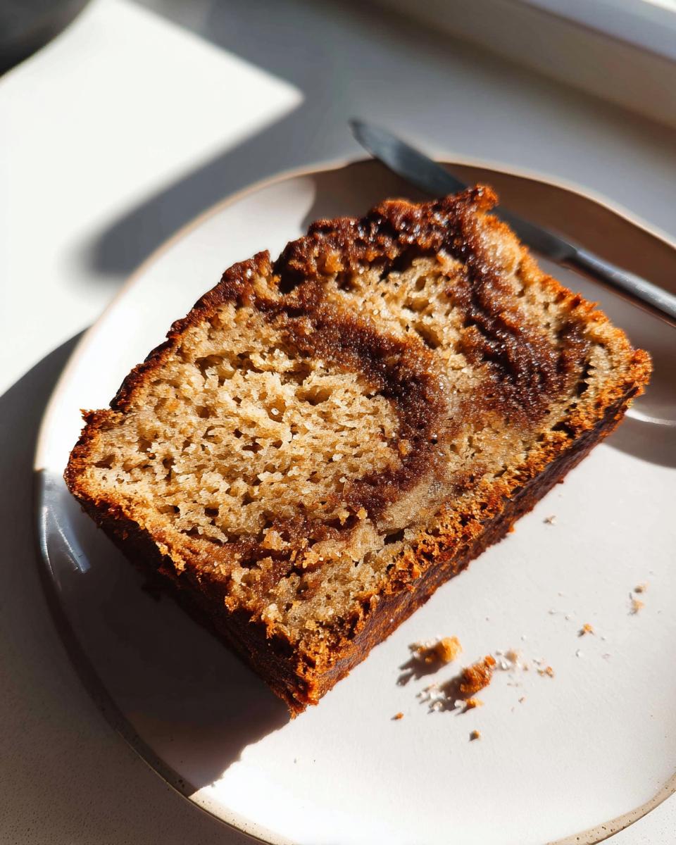 A close-up slice of moist Cinnamon Swirl Banana Bread with a rich brown swirl, served on a white plate.