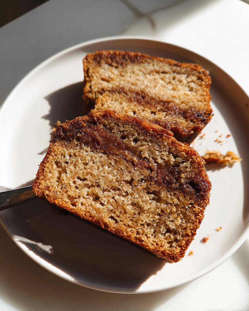 Two moist slices of Cinnamon Swirl Banana Bread showing a distinct brown cinnamon layer, served on a white plate.