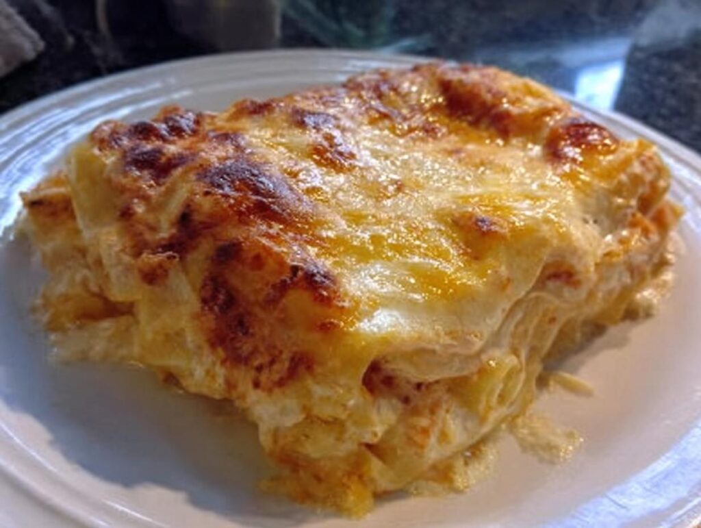 A close-up of a rich, layered slice of Extra Cheesy Four Cheese Lasagna with a golden, bubbly, baked cheese topping.