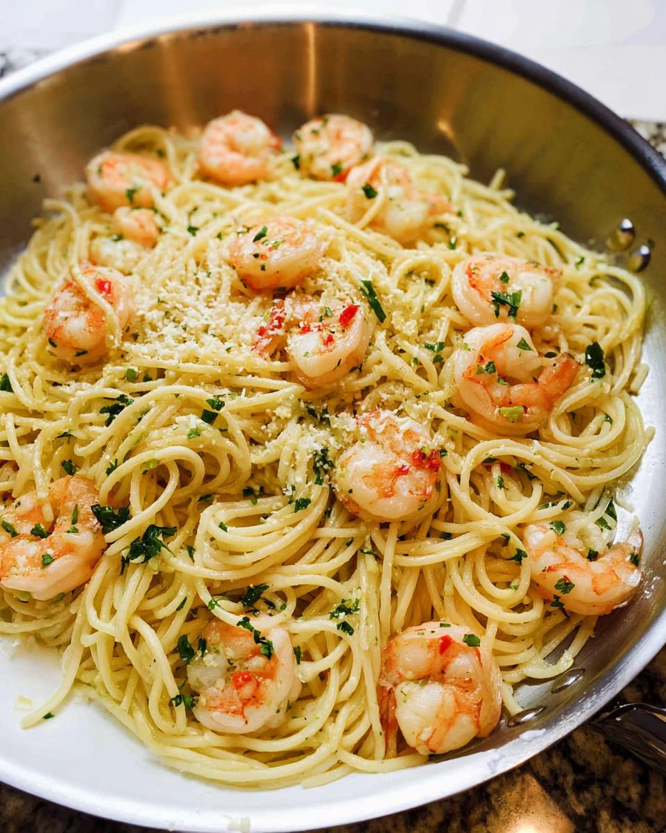 Close-up of Garlic Butter Shrimp Pasta tossed with shrimp, parsley, and grated cheese in a stainless steel skillet.