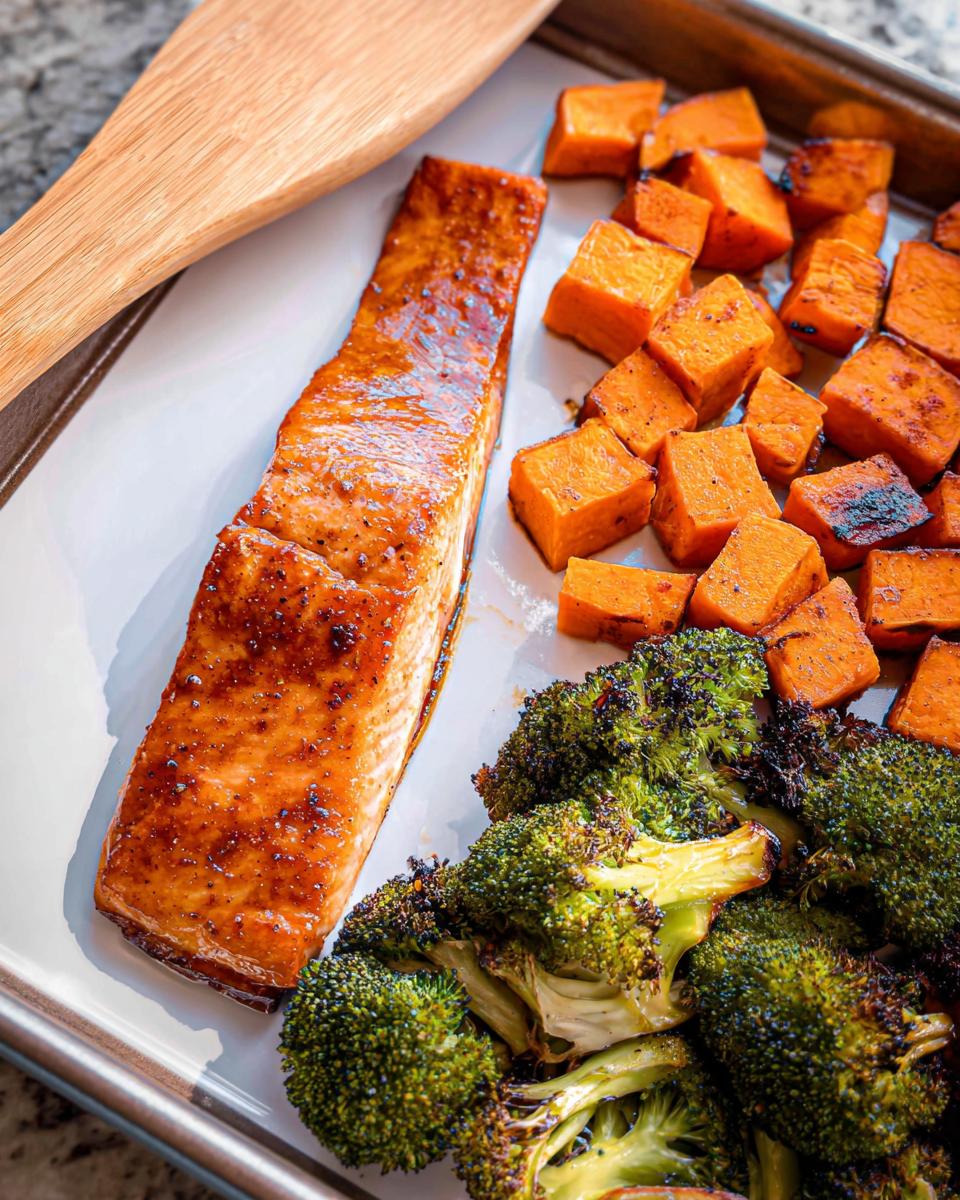 A glistening fillet of salmon glazed with maple dijon sauce next to roasted sweet potatoes and broccoli on a sheet pan.