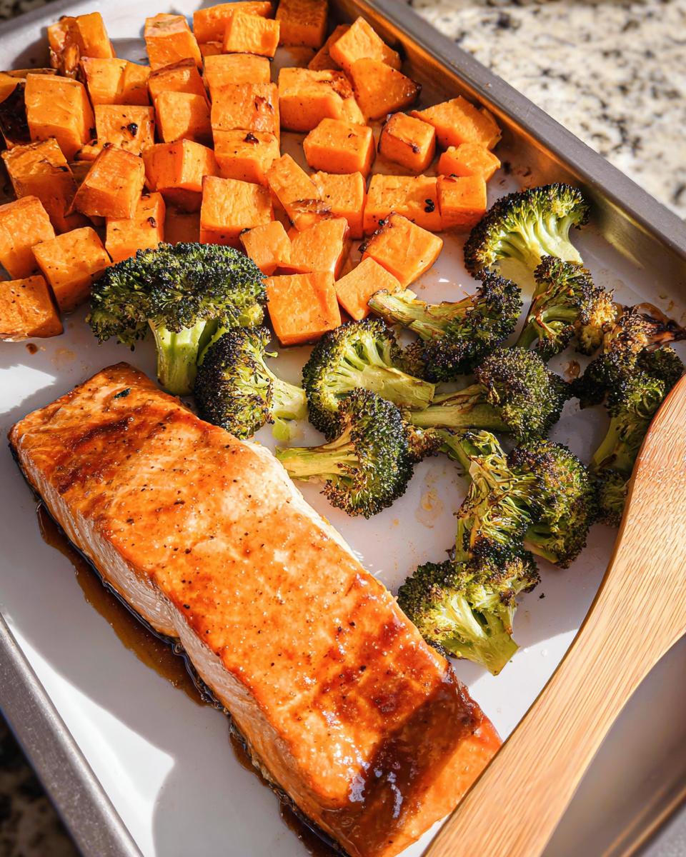 Glazed salmon fillet with roasted broccoli florets and diced sweet potatoes on a sheet pan for Maple Dijon Salmon Sheet Pan Dinner.