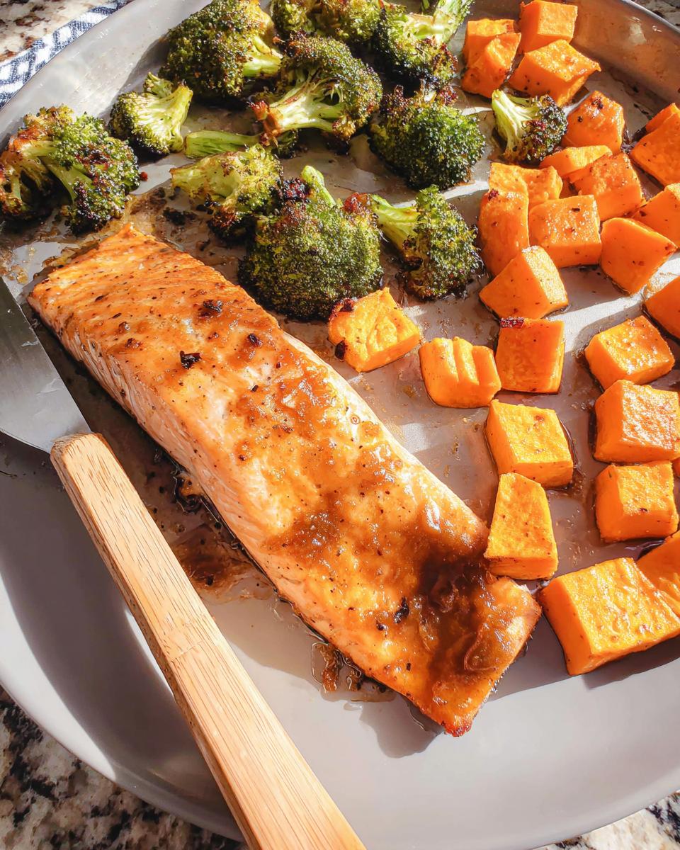 A perfectly cooked fillet of Maple Dijon Salmon Sheet Pan Dinner served with roasted broccoli and sweet potatoes on a baking sheet.
