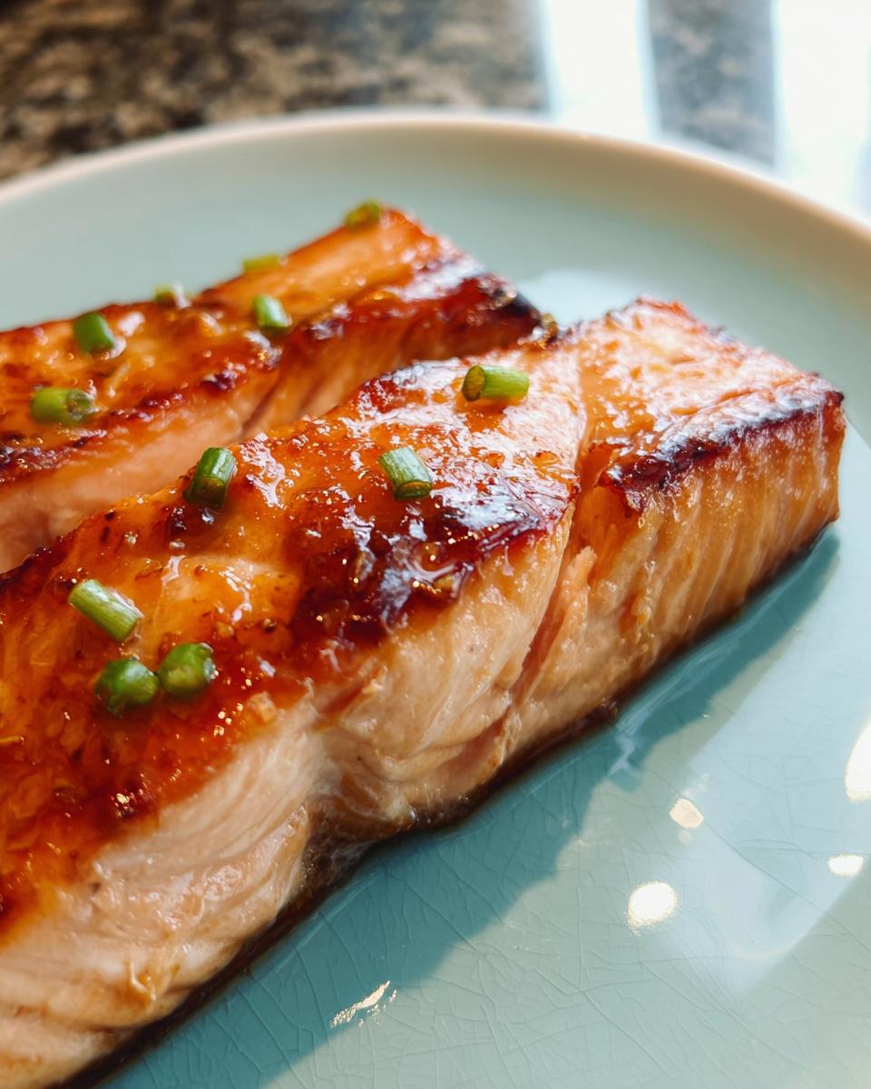 Two perfectly cooked fillets of Miso Glazed Broiled Salmon topped with chopped green onions on a light blue plate.
