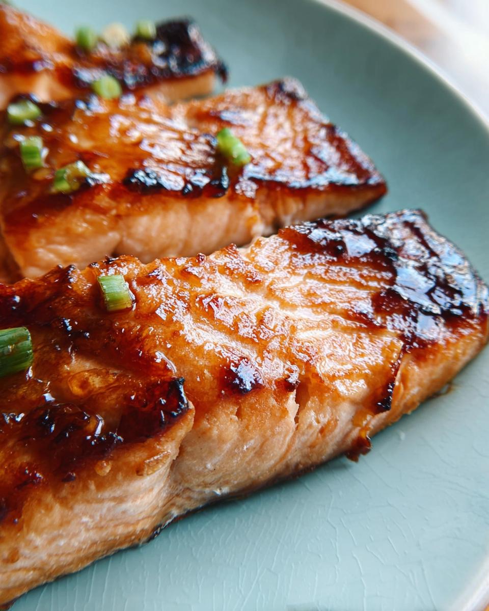 Close-up of perfectly cooked Miso Glazed Broiled Salmon fillets with a shiny glaze and green onion garnish.