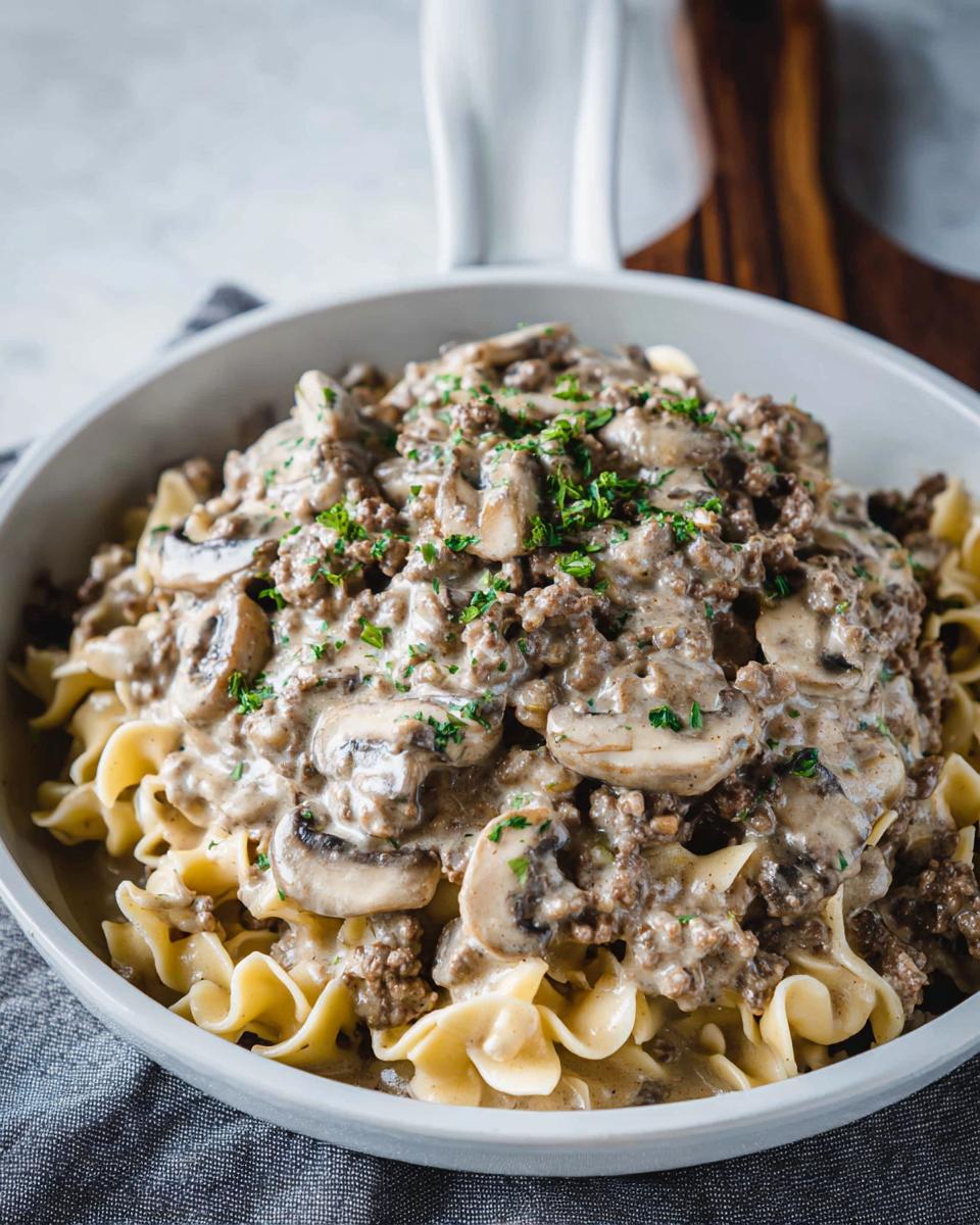 A close-up of One Pot Ground Beef Stroganoff served over egg noodles, topped with mushrooms and fresh parsley.