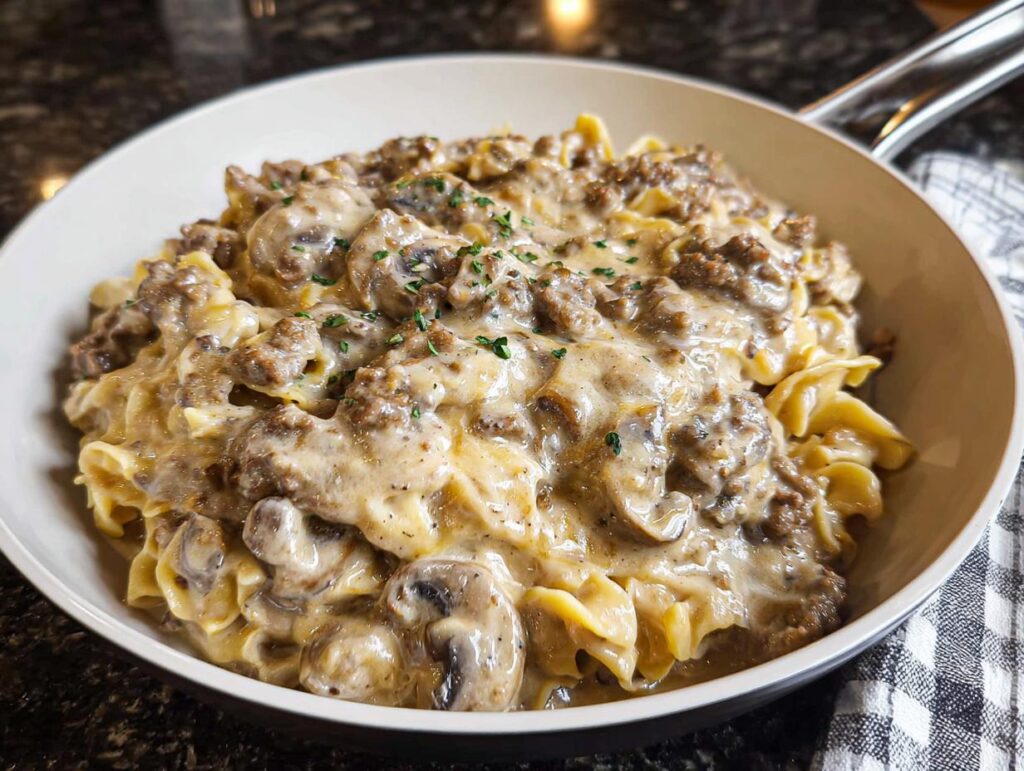 A close-up of creamy One Pot Ground Beef Stroganoff served in a light-colored skillet, topped with parsley.