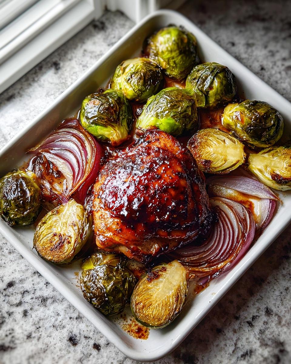 A close-up of Sheet Pan Balsamic Chicken and Brussels Sprouts glistening with glaze in a white baking dish.