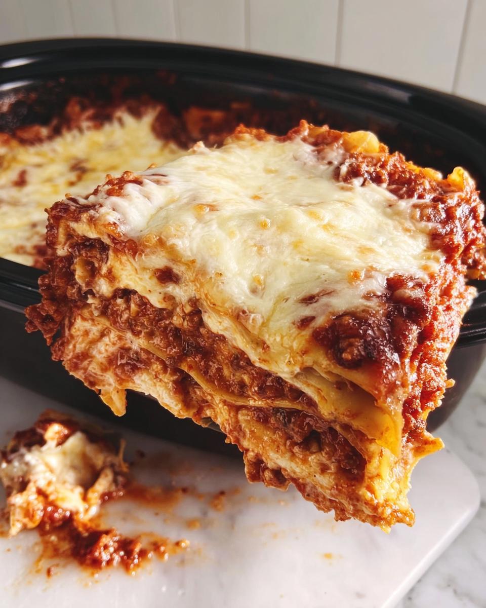 A thick, layered slice of Slow Cooker Lasagna with Meat Sauce topped with melted, bubbly cheese being lifted from the pot.