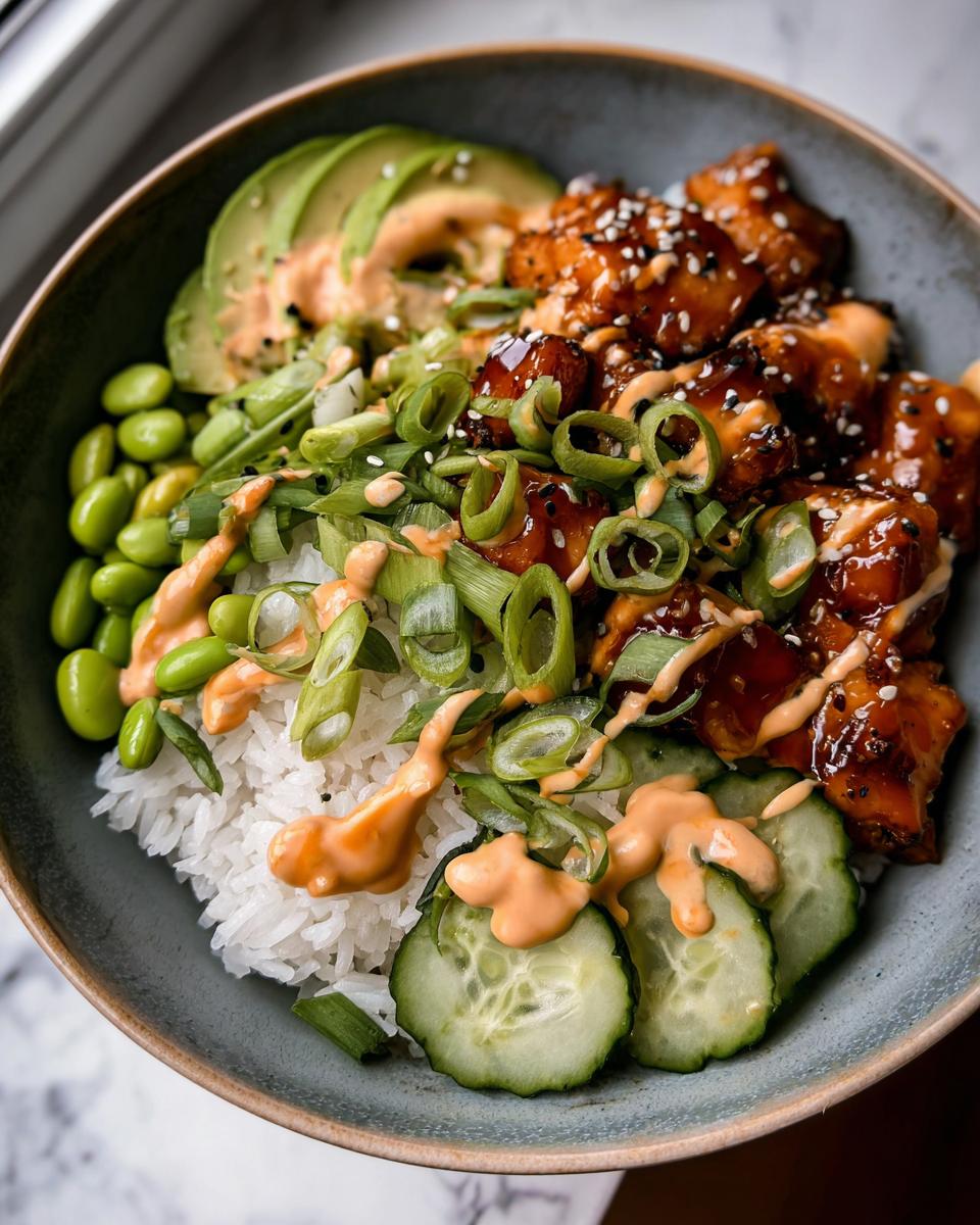 A close-up of a Teriyaki Glazed Salmon Rice Bowls featuring glazed salmon, rice, avocado, edamame, and spicy mayo drizzle.
