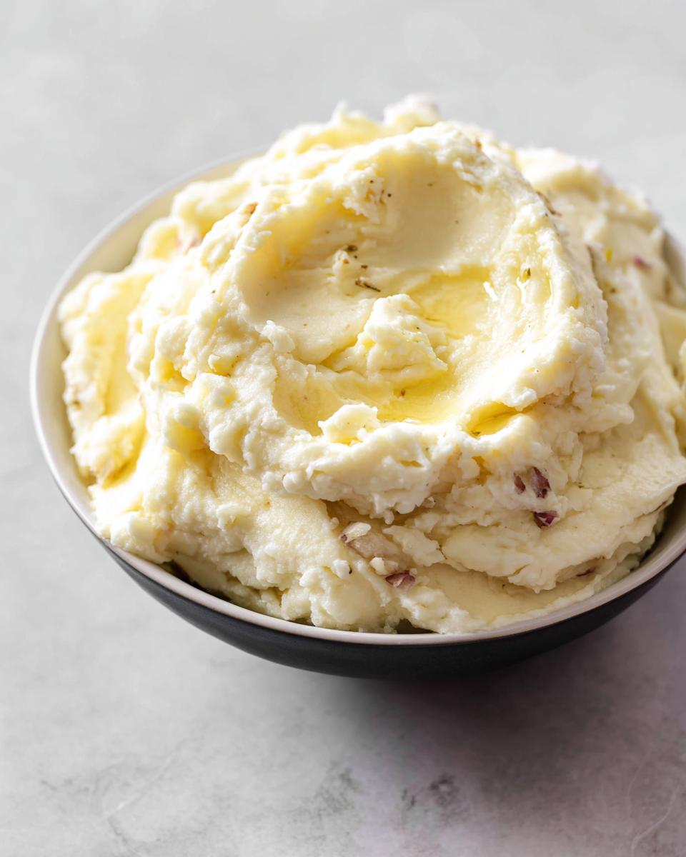 A close-up of a bowl filled with fluffy Ultra Creamy Garlic Mashed Potatoes, topped with melted butter.