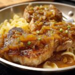 Close-up of 10-ingredient pork chops smothered in a rich onion sauce, served over egg noodles.