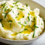 A close-up of creamy 12-ingredient mashed potatoes topped with melted butter and fresh chives.