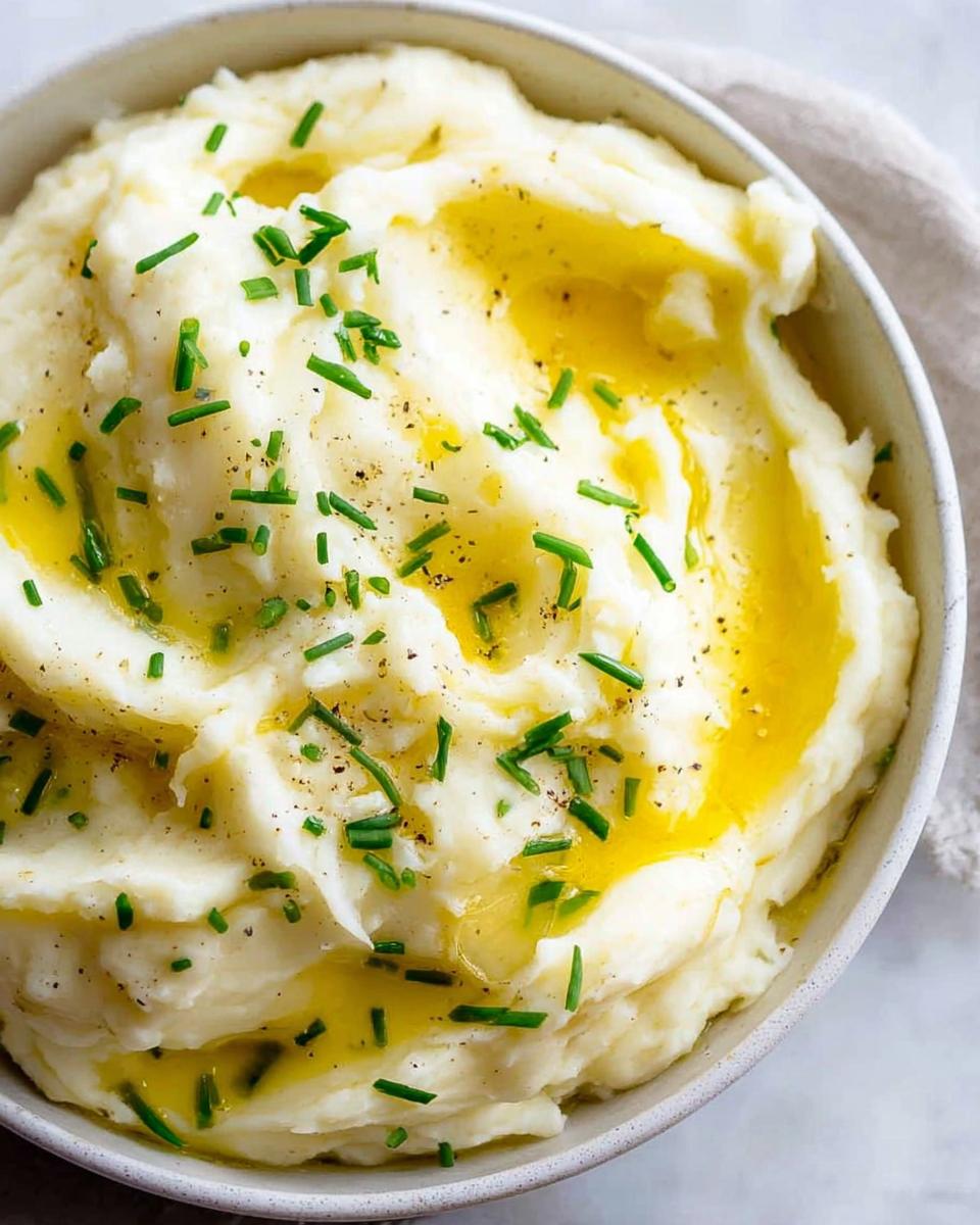 A close-up of fluffy 12-Ingredient Mashed Potatoes topped with melted butter and fresh chives.